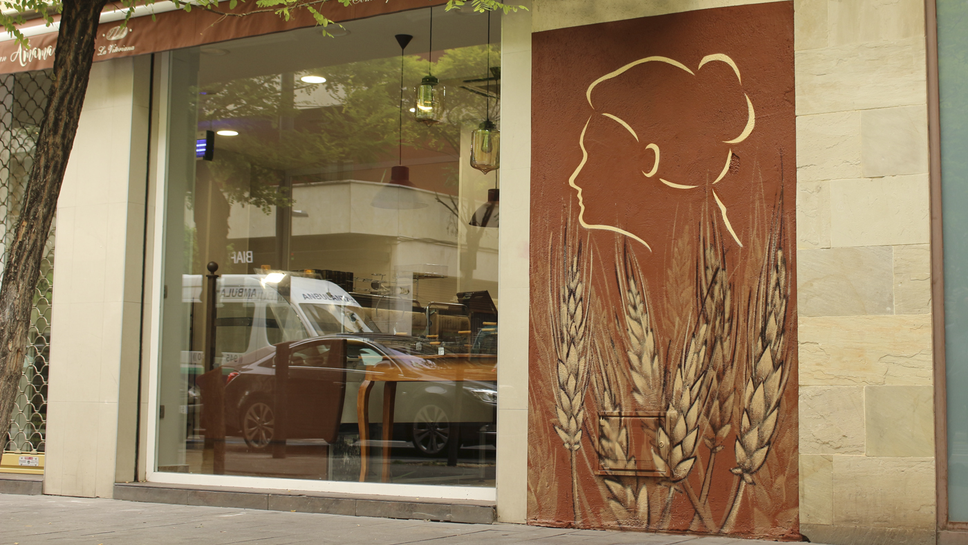 Pintura mural realizada por Ha13estudio en Vitoria Gasteiz, el mural decora la fachada de la panadería pastelería con unas espigas de trigo y la silueta de una mujer representativa de la imagen de la empresa La Vitoriana