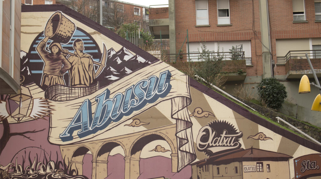 Mural de Abusu en el que aparecen pintados una pareja de mineros el antiguo puente y unas letras con el nombre de Abusu.