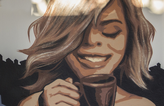 Pintura mural realizada por Ha13estudio de una chica tomando café.